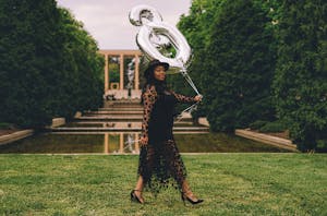 Trendy black woman walking near water with balloons in shape of number 30