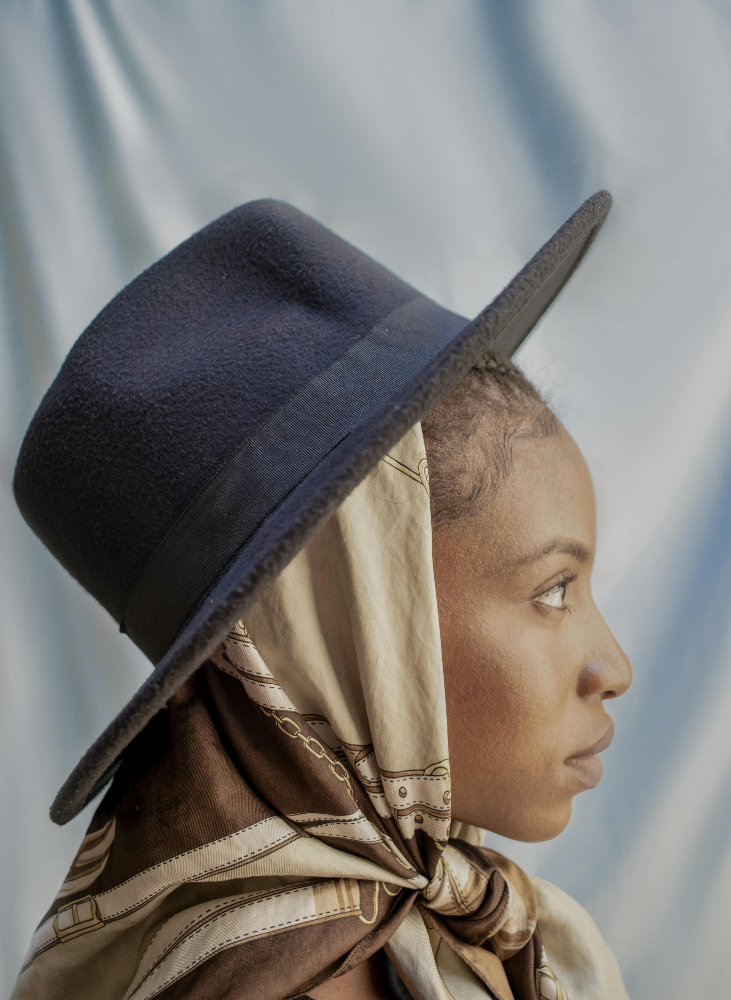 Profile portrait of a woman wearing a hat and scarf against a soft background