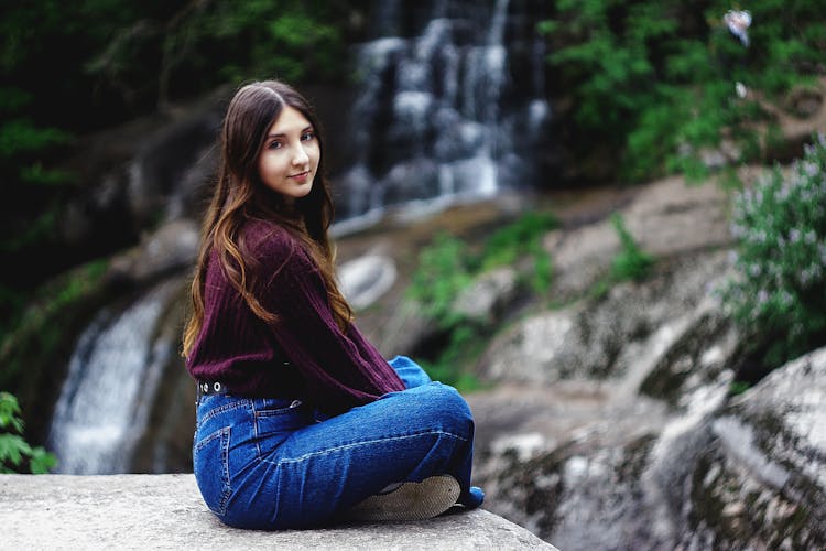 Woman In Purple Long Sleeve Shirt And Blue Denim Jeans Sitting On Gray Surface