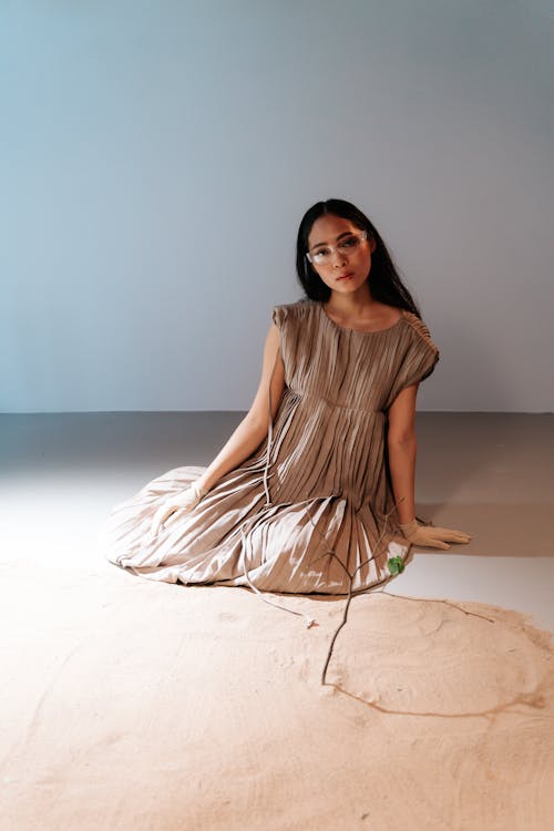 A Woman in Brown Dress Sitting on the Floor Near the Sand