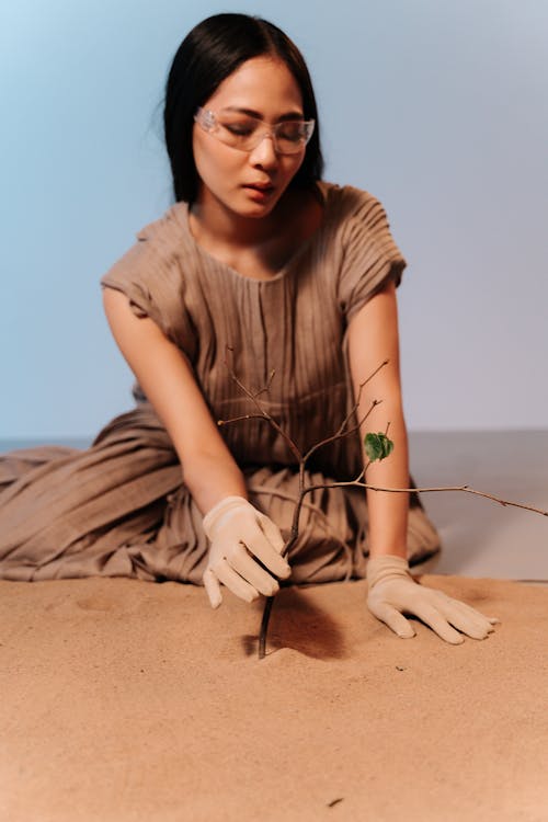 A Woman Wearing Gloves while Holding a Tree Branches on the Sand