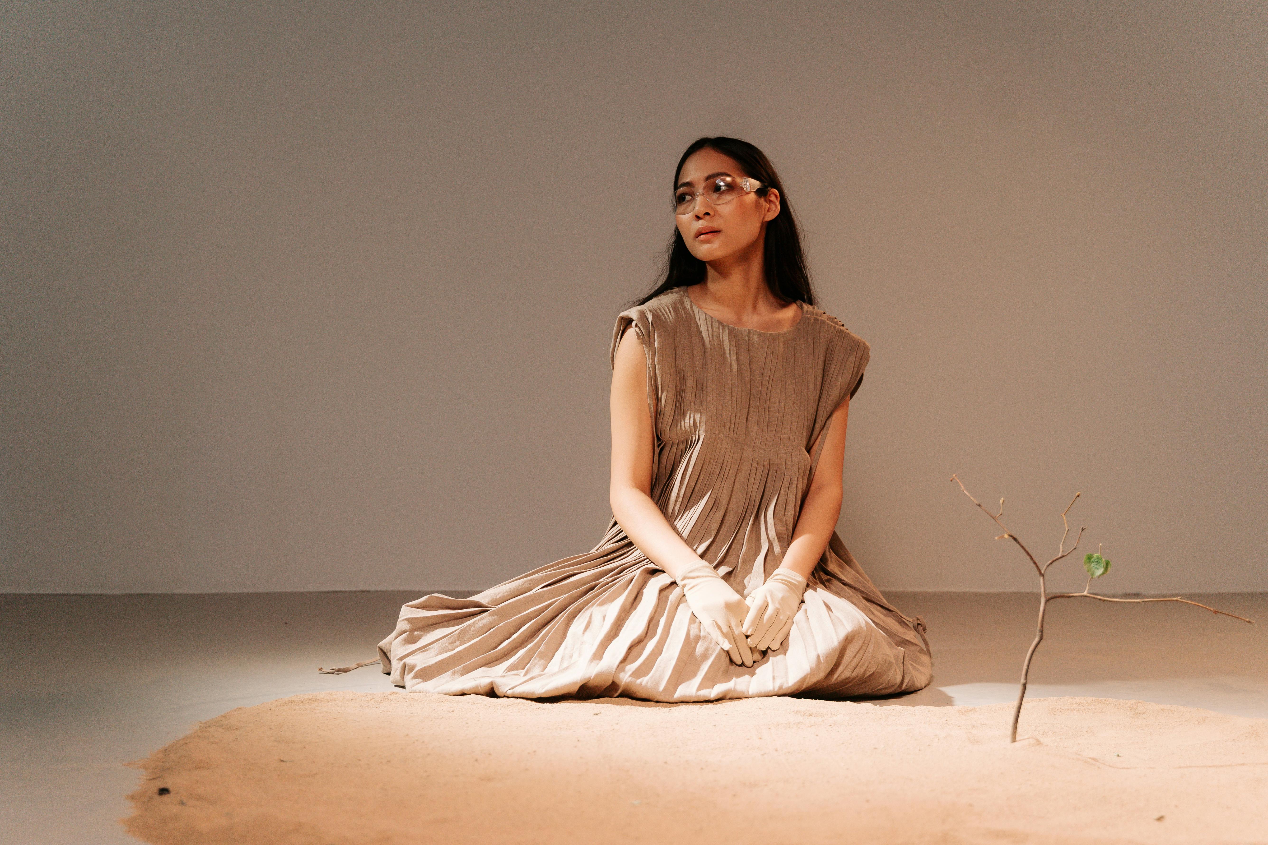 Woman in a brown dress sits in a minimalist studio, symbolizing climate change.