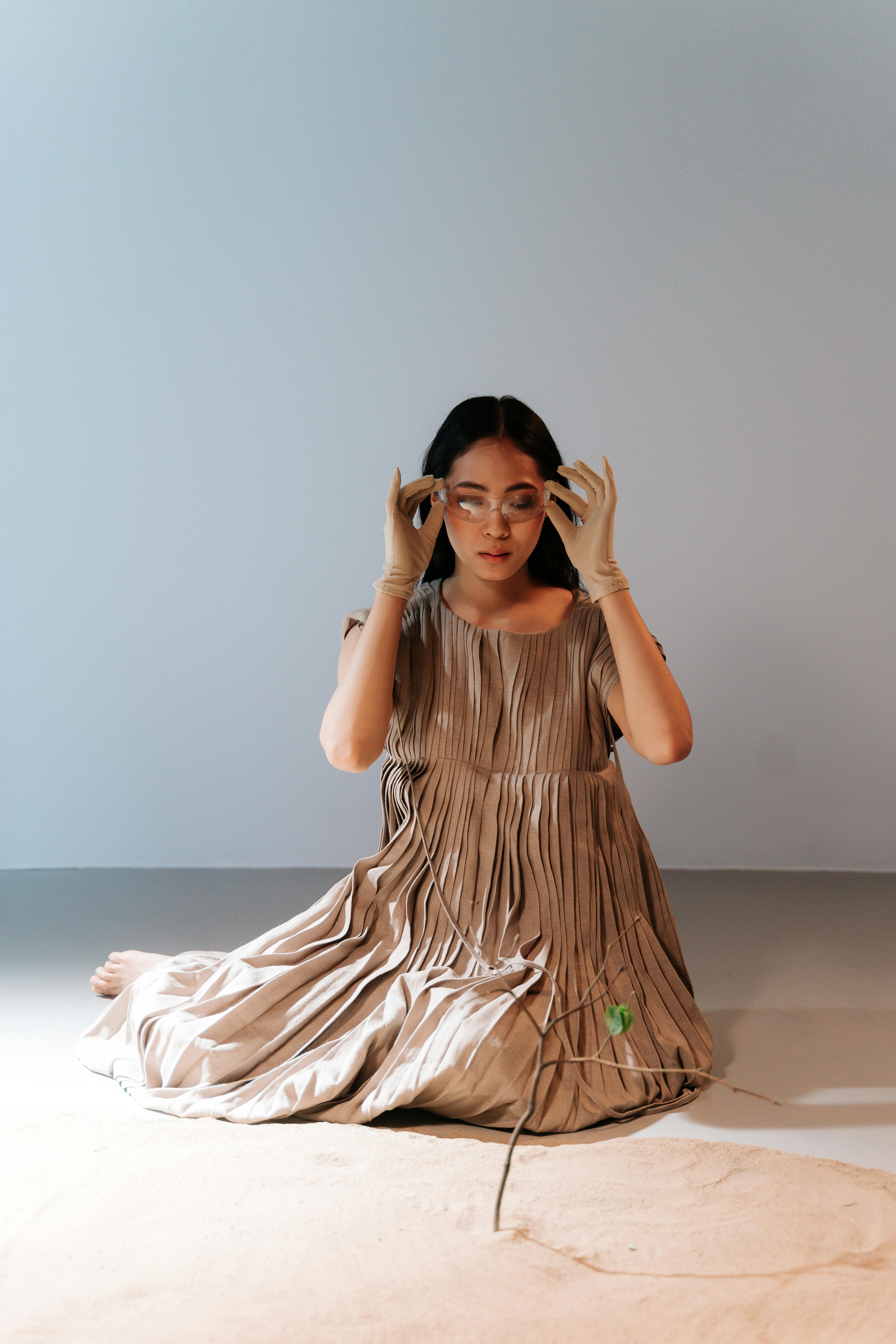 a woman in brown dress sitting near the sand while holding her goggles