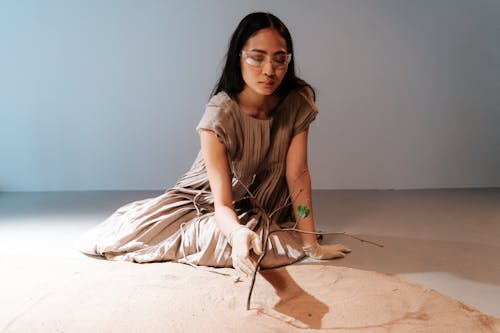 A Woman Sitting Near the Sand while Holding a Tree Branches