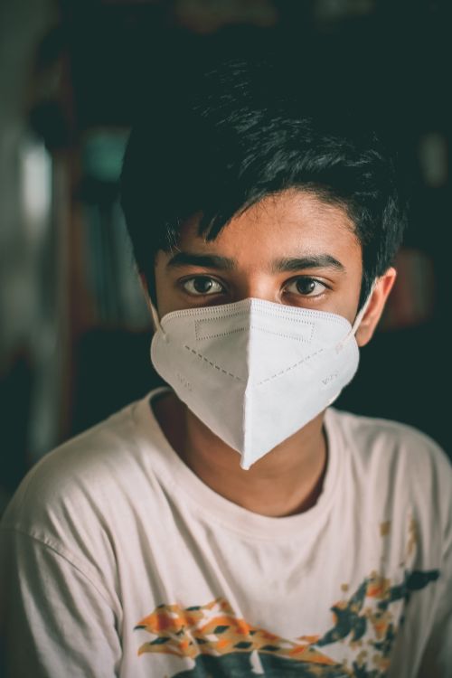 Free Teen boy wearing a white face mask indoors, highlighting COVID-19 safety measures. Stock Photo