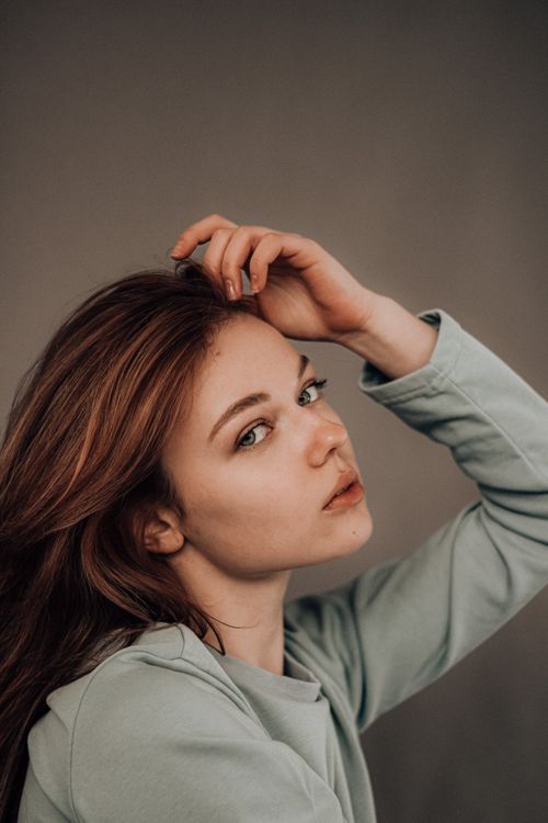 Free Young dreamy female model with long dark hair and makeup in gray sweatshirt looking at camera hand touching head Stock Photo