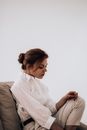 Side view of young sad female with trendy hairstyle wearing elegant white outfit resting on couch looking down