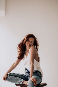 Young smiling female in casual clothes with long dark wavy hair sitting on chair looking at camera against white background