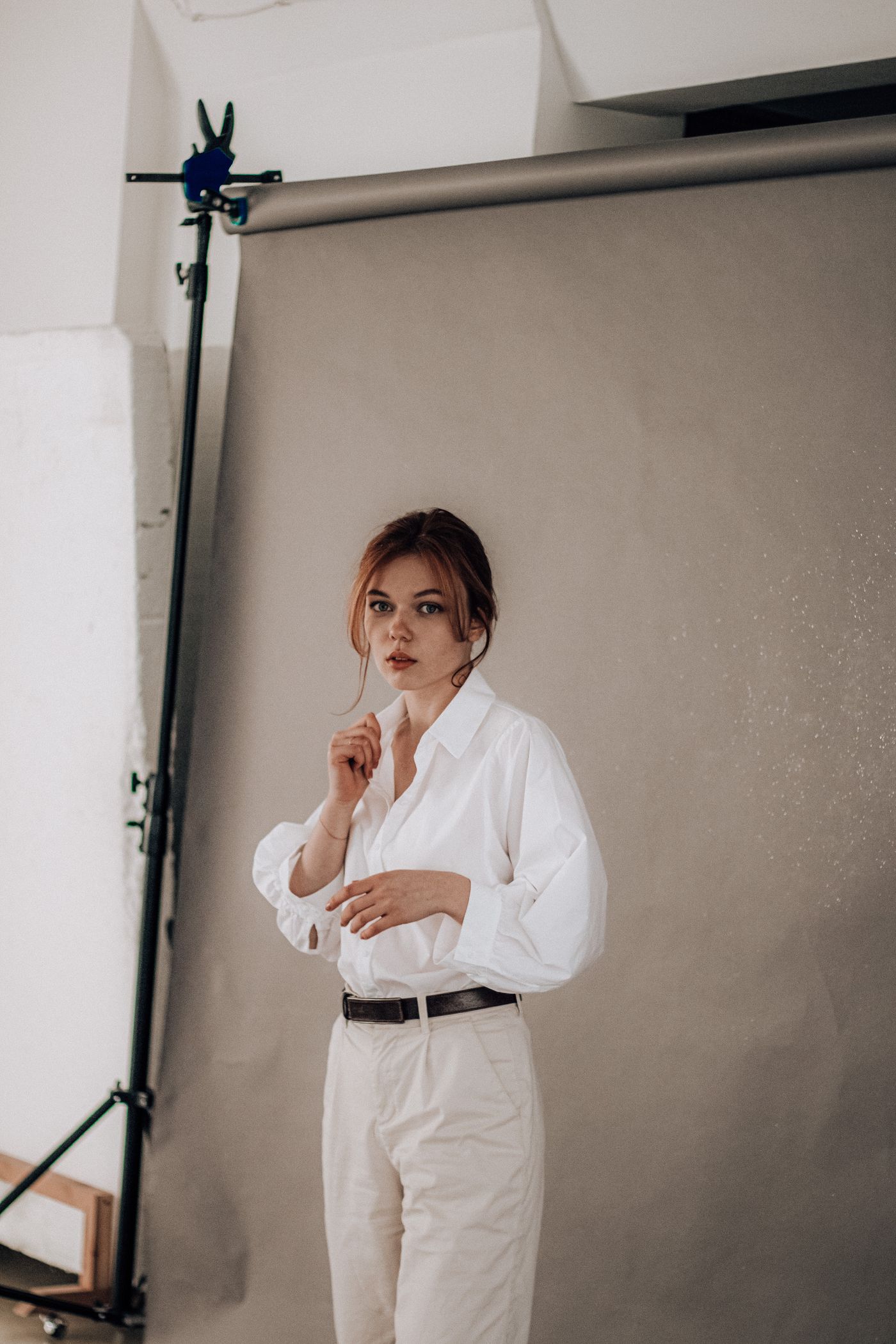 Woman wearing a white button-front shirt and pale trousers against a studio backdrop.