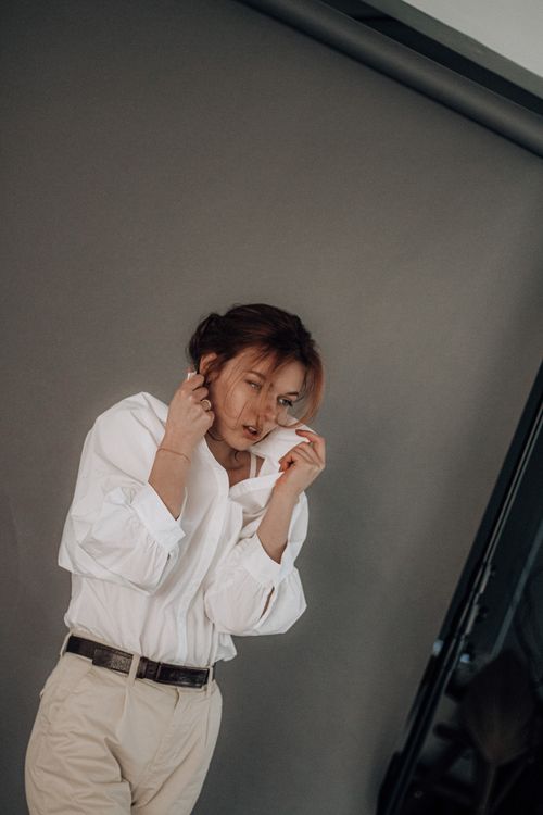Free Young female touching raised collar of white shirt with hands while shooting on brown photo screen in studio Stock Photo