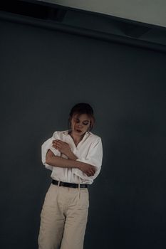 Positive female model wearing oversize white shirt and beige trousers shooting on gray screen in studio