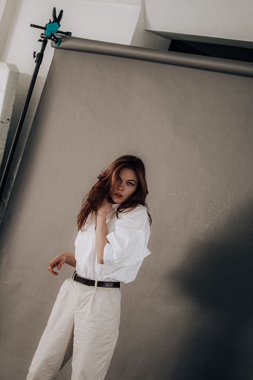 Free Young confident female with dark wavy hair wearing white shirt and light trousers shooting on gray studio screen Stock Photo