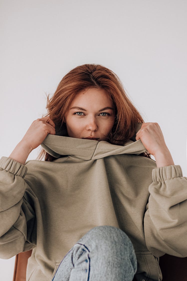 Young Woman In Hoodie And Jeans Sitting With Bent Leg