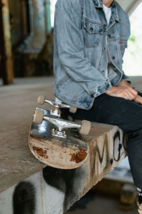 Free A skateboarder in a denim jacket sitting on a graffiti-covered ramp with skateboard. Stock Photo