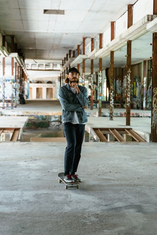 Free A male skater stands on his skateboard inside a graffiti-filled abandoned building. Stock Photo