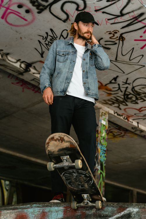Free Stylish man in denim jacket with skateboard in graffiti-covered skate park. Stock Photo
