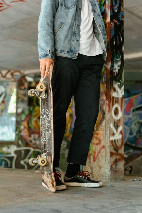 Free A cool skater holding a skateboard in a graffiti-covered urban space, expressing youth culture. Stock Photo