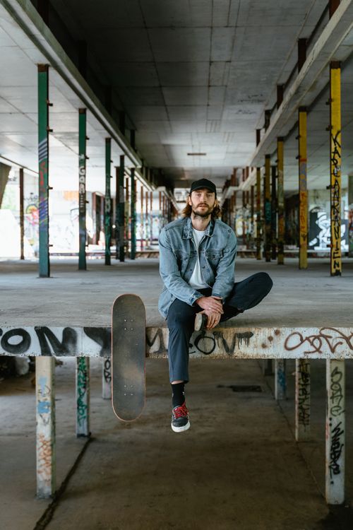 Free Young man with skateboard sitting in urban graffiti-filled skate park. Stock Photo