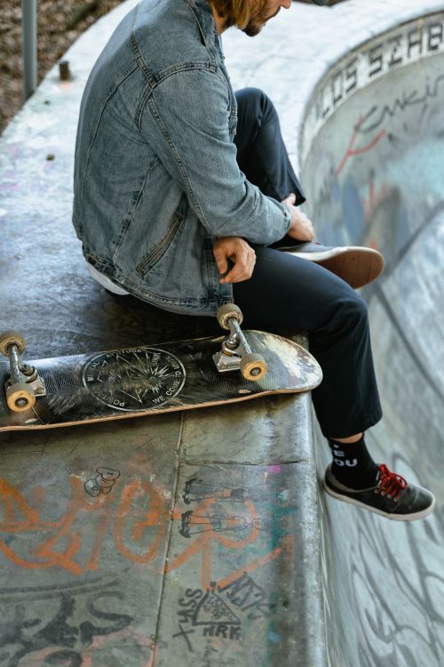Free Young man in denim jacket at skate park resting on a skate ramp with his skateboard Stock Photo