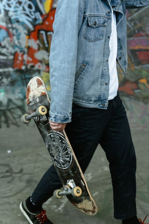 Free A close-up shot of a skateboarder holding a skateboard, wearing a denim jacket, with graffiti background. Stock Photo