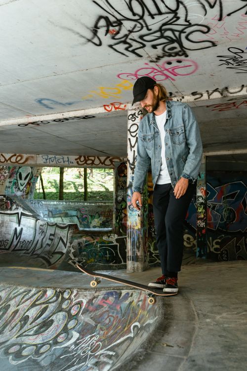 Free A man in a denim jacket skateboards in a graffiti-covered park, exuding urban style. Stock Photo