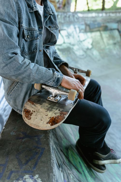 Free A skateboarder in a denim jacket sits holding a skateboard in an urban skatepark. Youth and lifestyle concept. Stock Photo