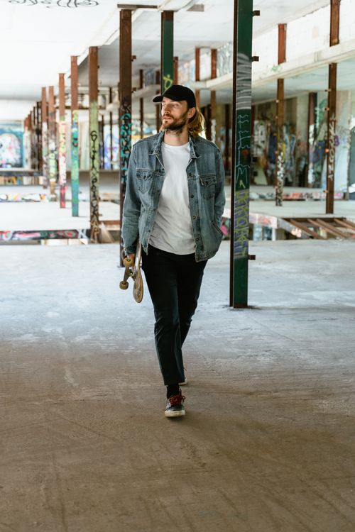 Free Man walks through a graffiti-filled warehouse holding a skateboard, exuding a stylish urban vibe. Stock Photo