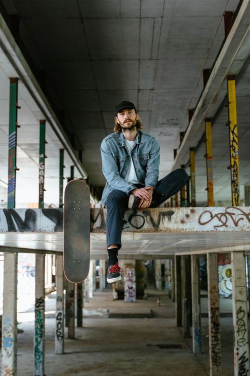 Free Male skateboarder in denim next to board, amidst graffiti, in urban environment. Stock Photo