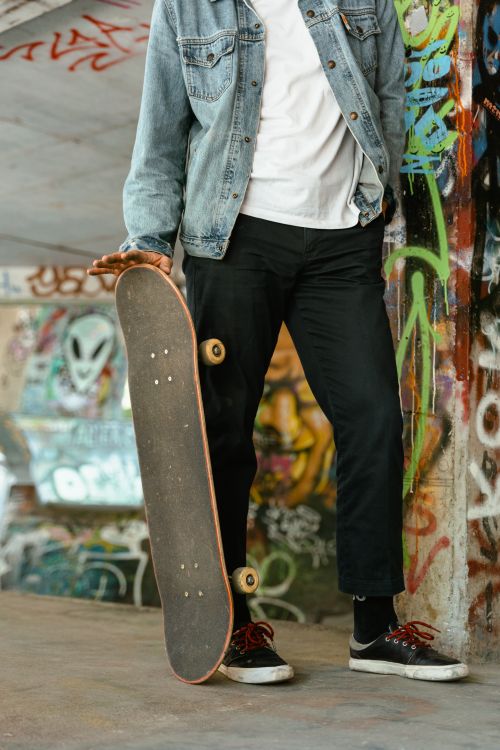 Free Casual skater posing with a skateboard in a vibrant graffiti-covered skatepark. Perfect for urban culture themes. Stock Photo