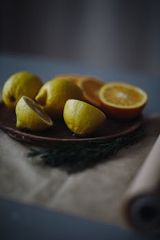 Whole and cut fresh lemons placed on brown plate against dark blurred background