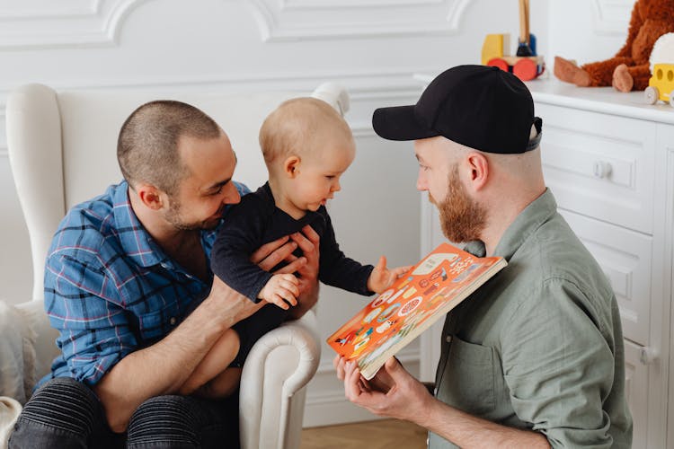 A Same Sex Couple Taking Care Of Their Child While Showing A Book