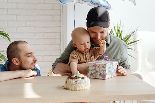 A Man Holding His Son while Unwrapping the Gift on the Table