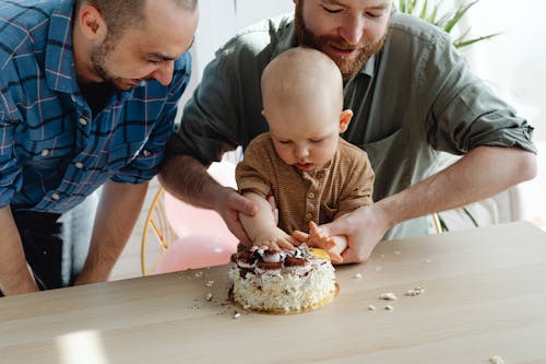 A Same Sex Couple Looking at Their Son Touching the Cake