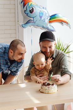 Father and son celebrate birthday with cake and character balloon indoors.