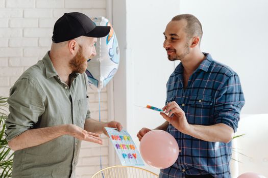 Two men celebrating a birthday indoors with balloons and smiles.