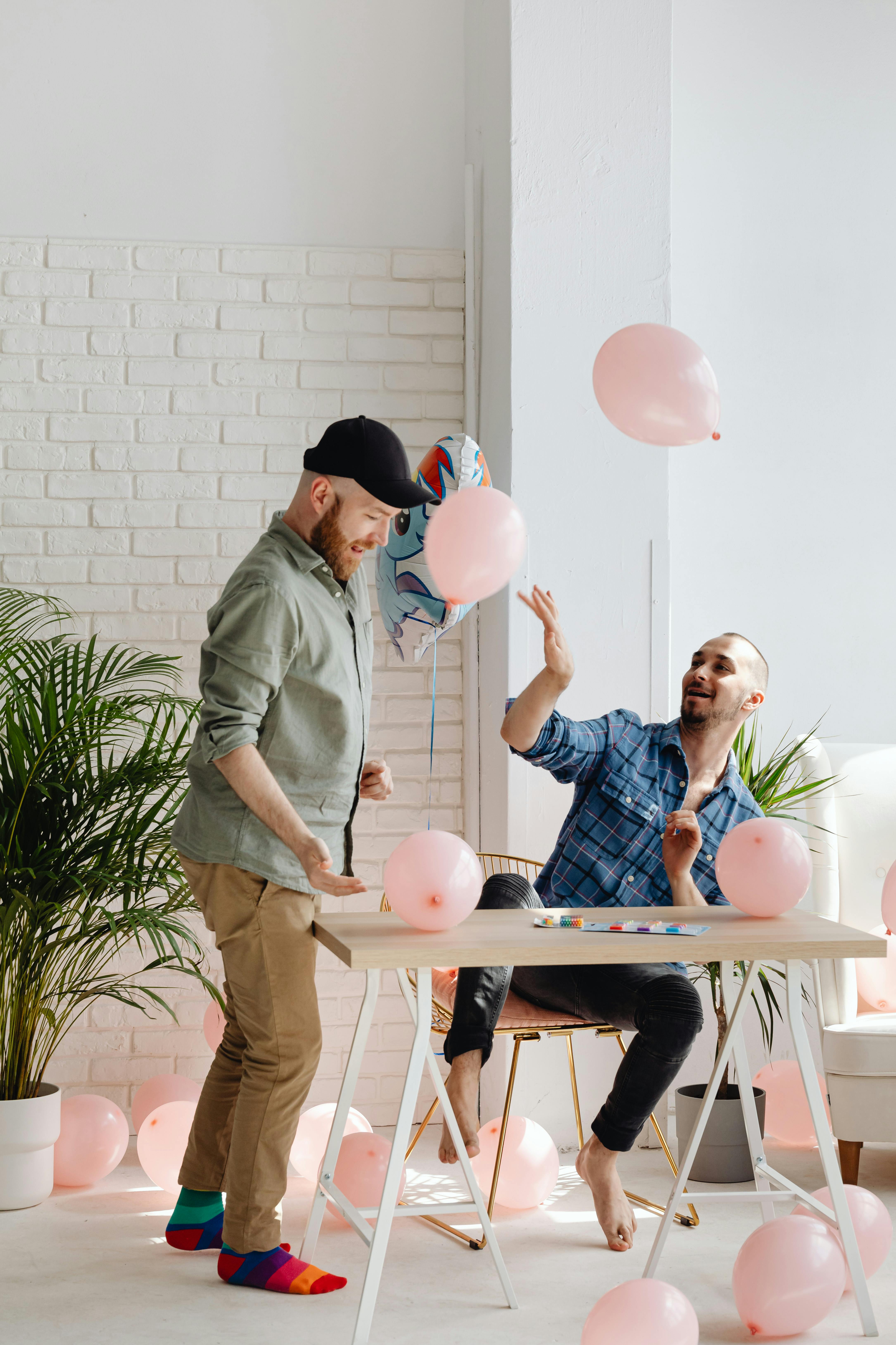 A lively indoor scene of two adults celebrating with pink balloons and laughter.