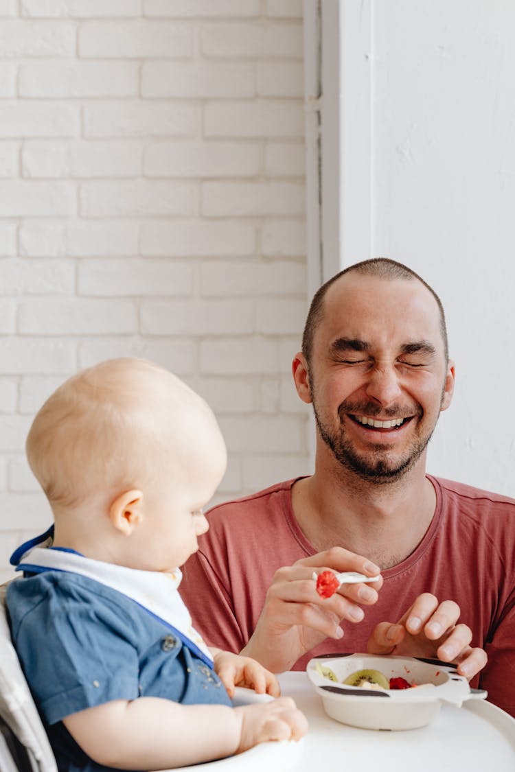 Man In Red Crew Neck Shirt Feeding A Baby