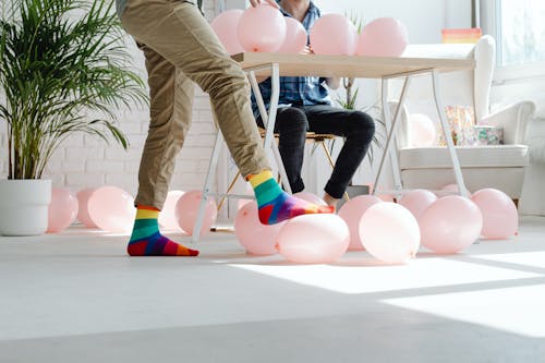 Person in Colorful Socks Stepping on Pink Balloon