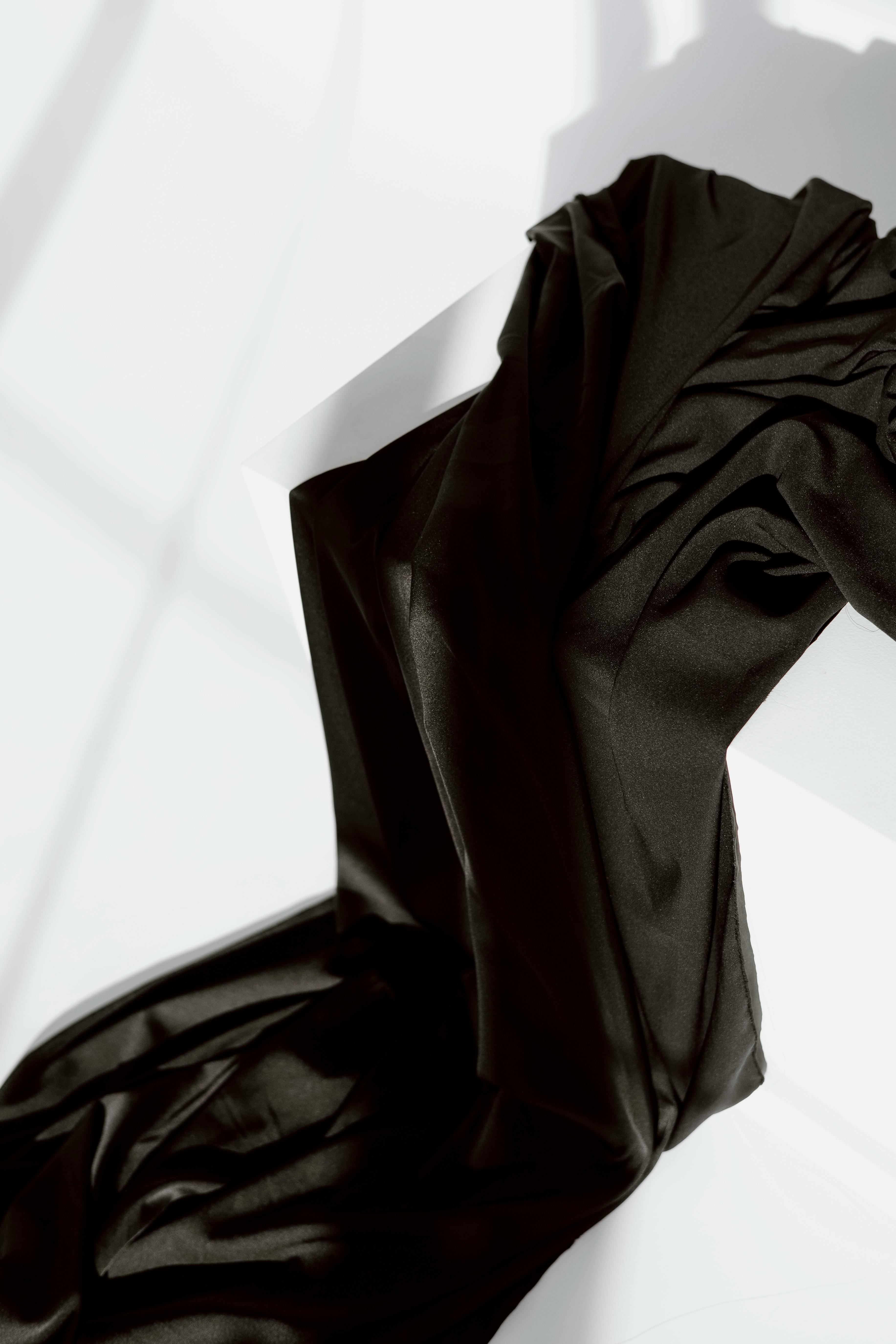 Close-up of luxurious black textile draped over a minimalistic white box with soft shadows.