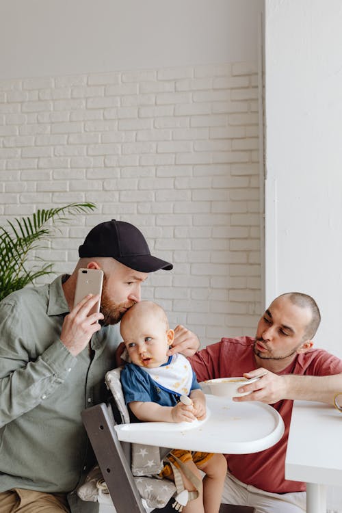 Man on Cellphone Kissing Baby on High Chair