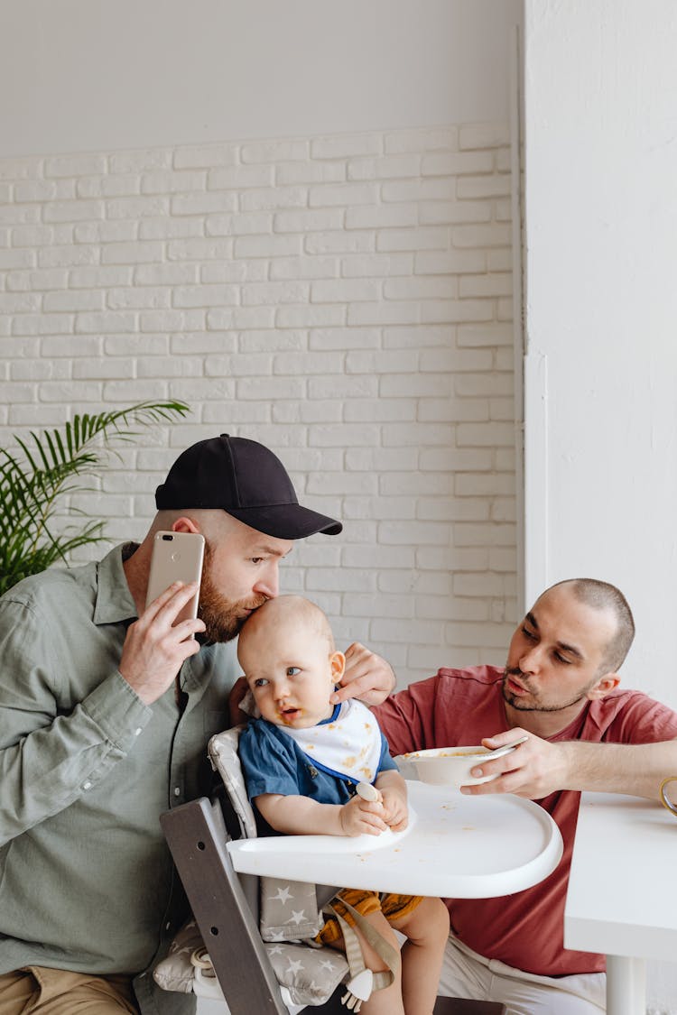 Man On Cellphone Kissing Baby On High Chair