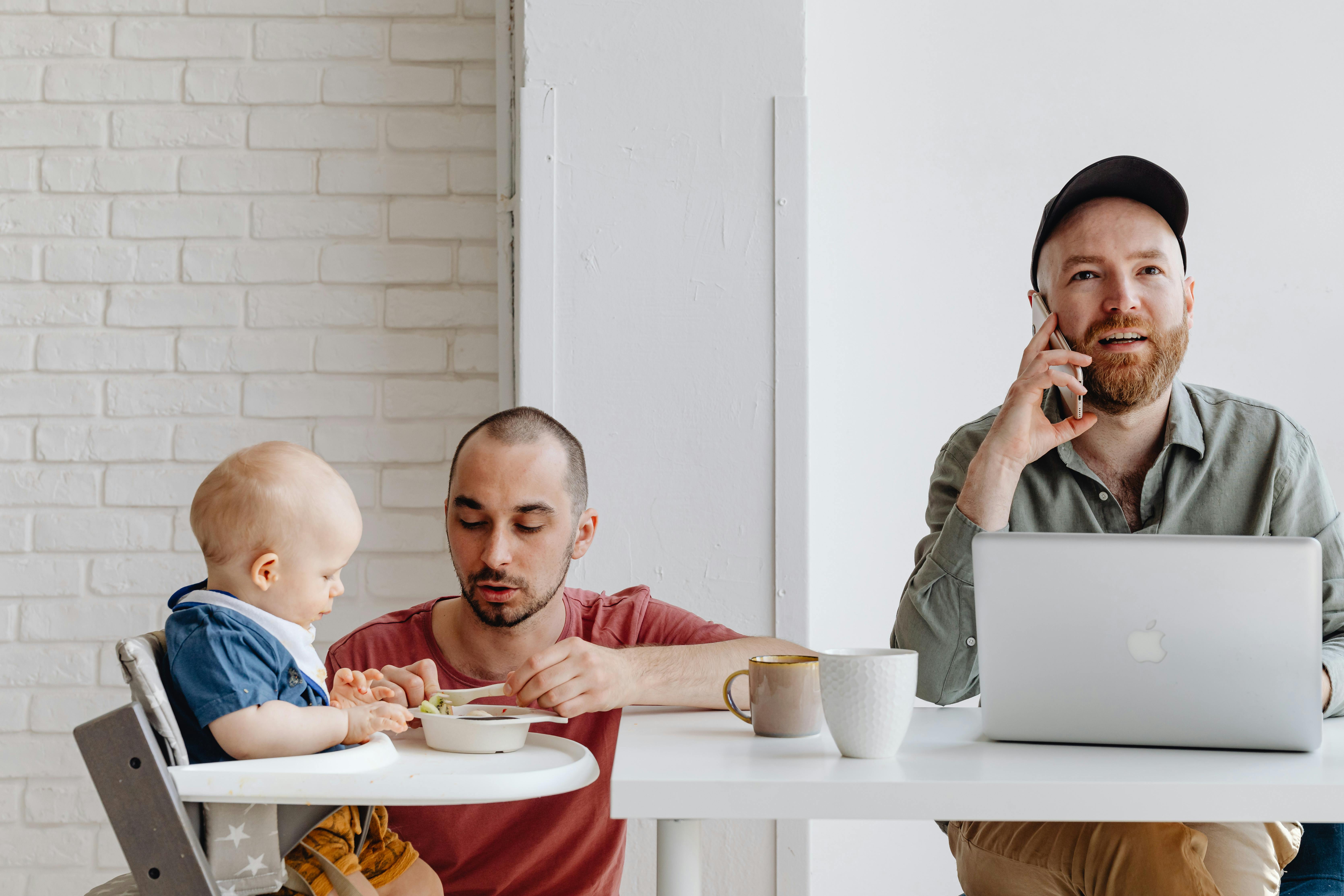 father feeding a baby next to his partner working on a laptop