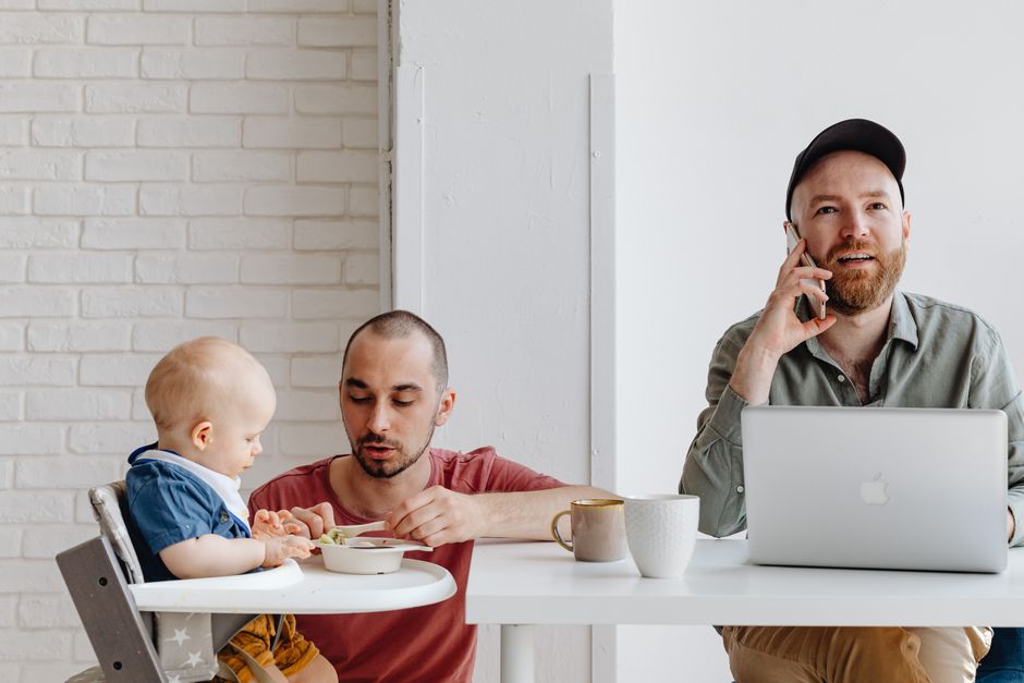Feliz pareja gay con su bebé disfrutando de una comida y trabajo en casa.