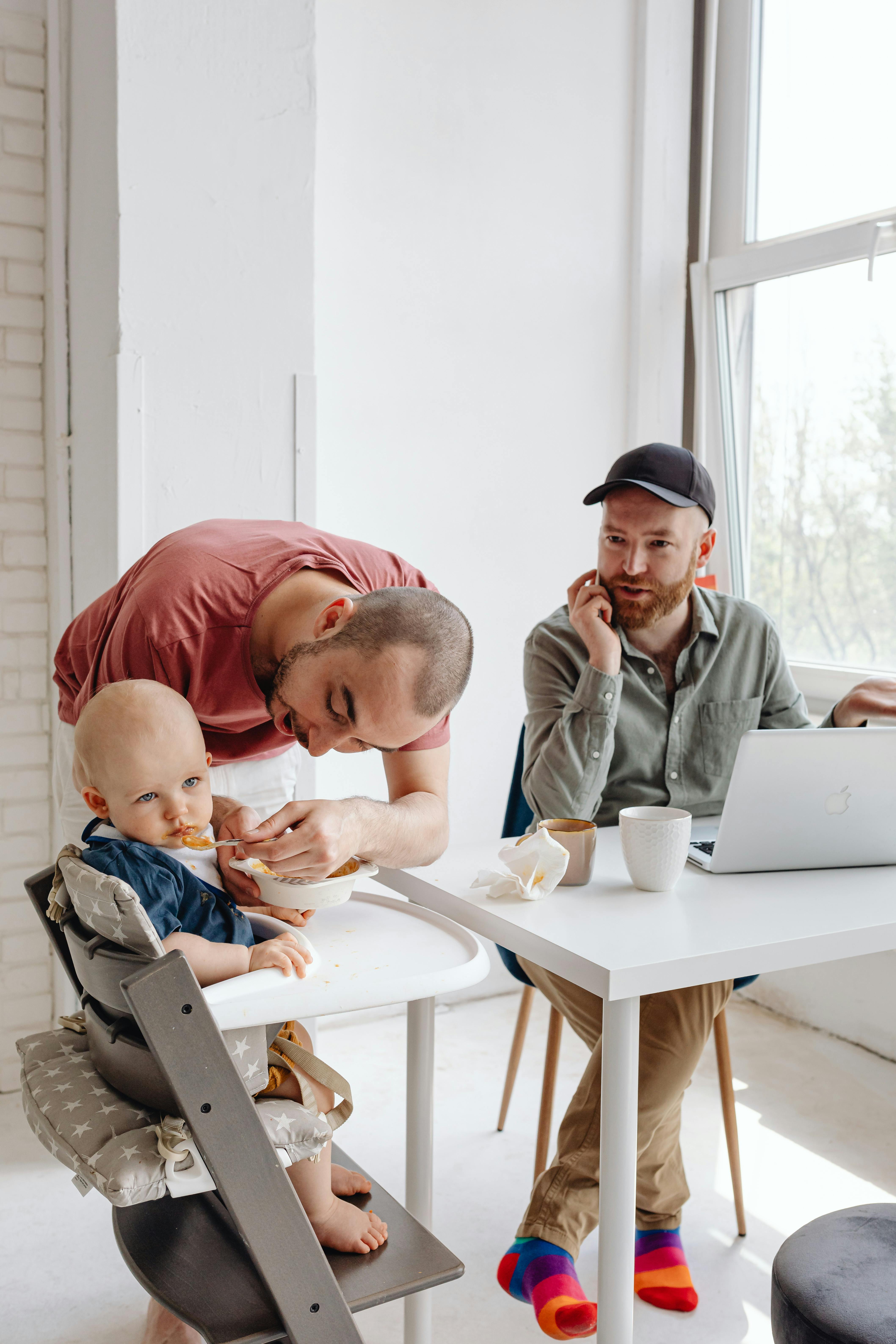 man in pink shirt feeding baby sitting on high chair