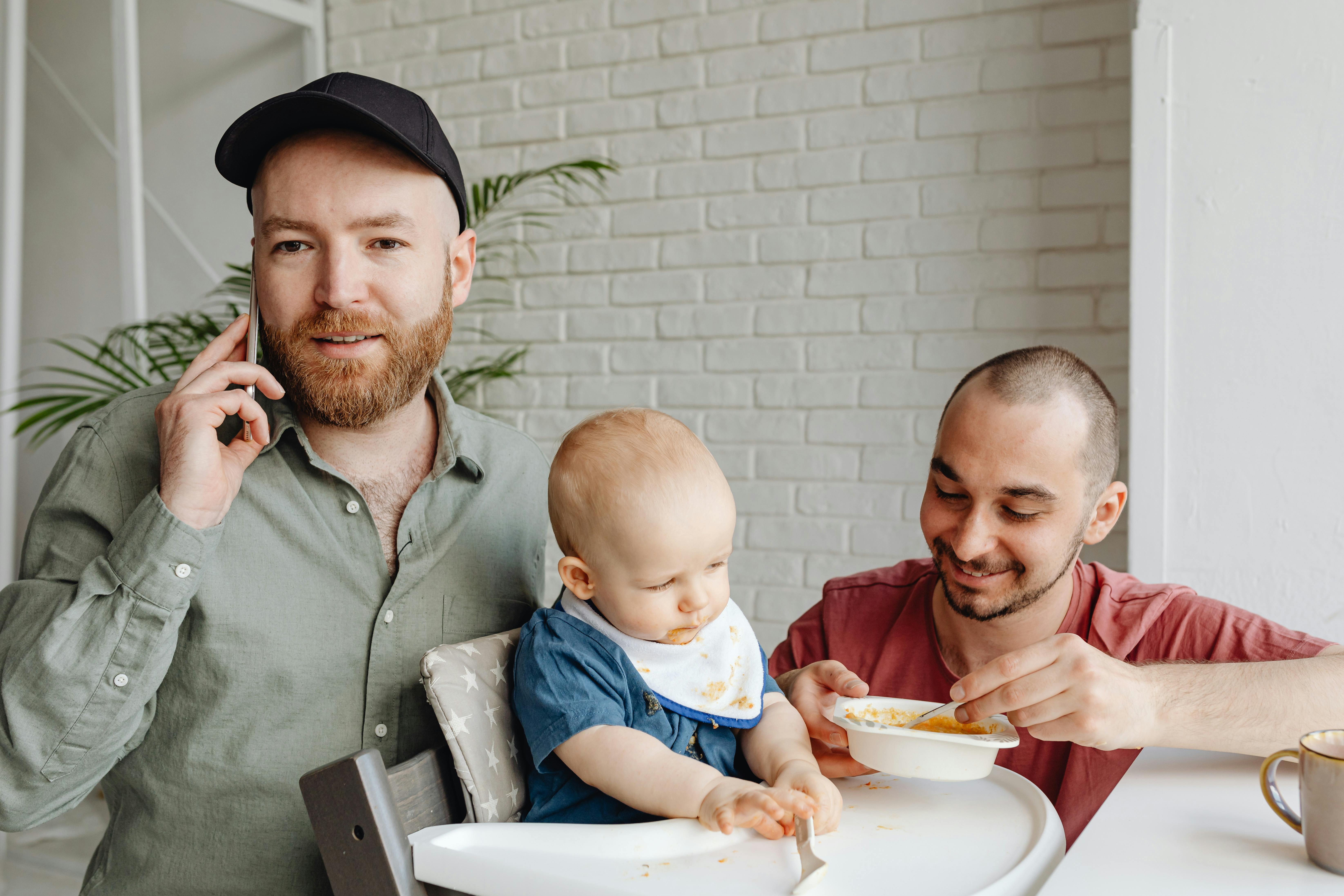 father feeding baby next to his partner talking on the phone