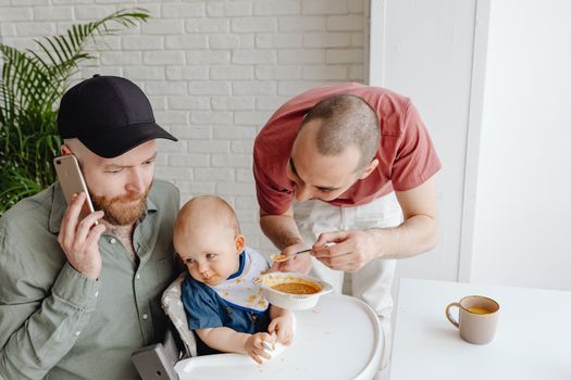Father Talking on the Phone Next to a Fussy Baby Spoon-fed by His Father