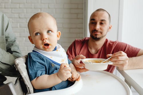 Man in Red Crew Neck Shirt Feeding a Baby