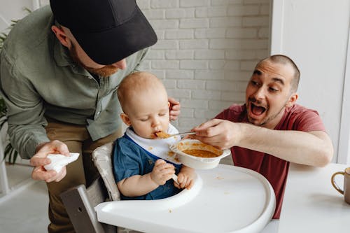 Free Man in Red Shirt Feeding Baby on a High Chair Stock Photo