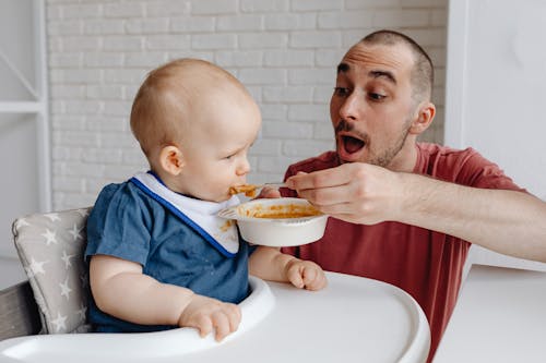 Free Man in Blue Shirt Holding Baby in White High Chair Stock Photo