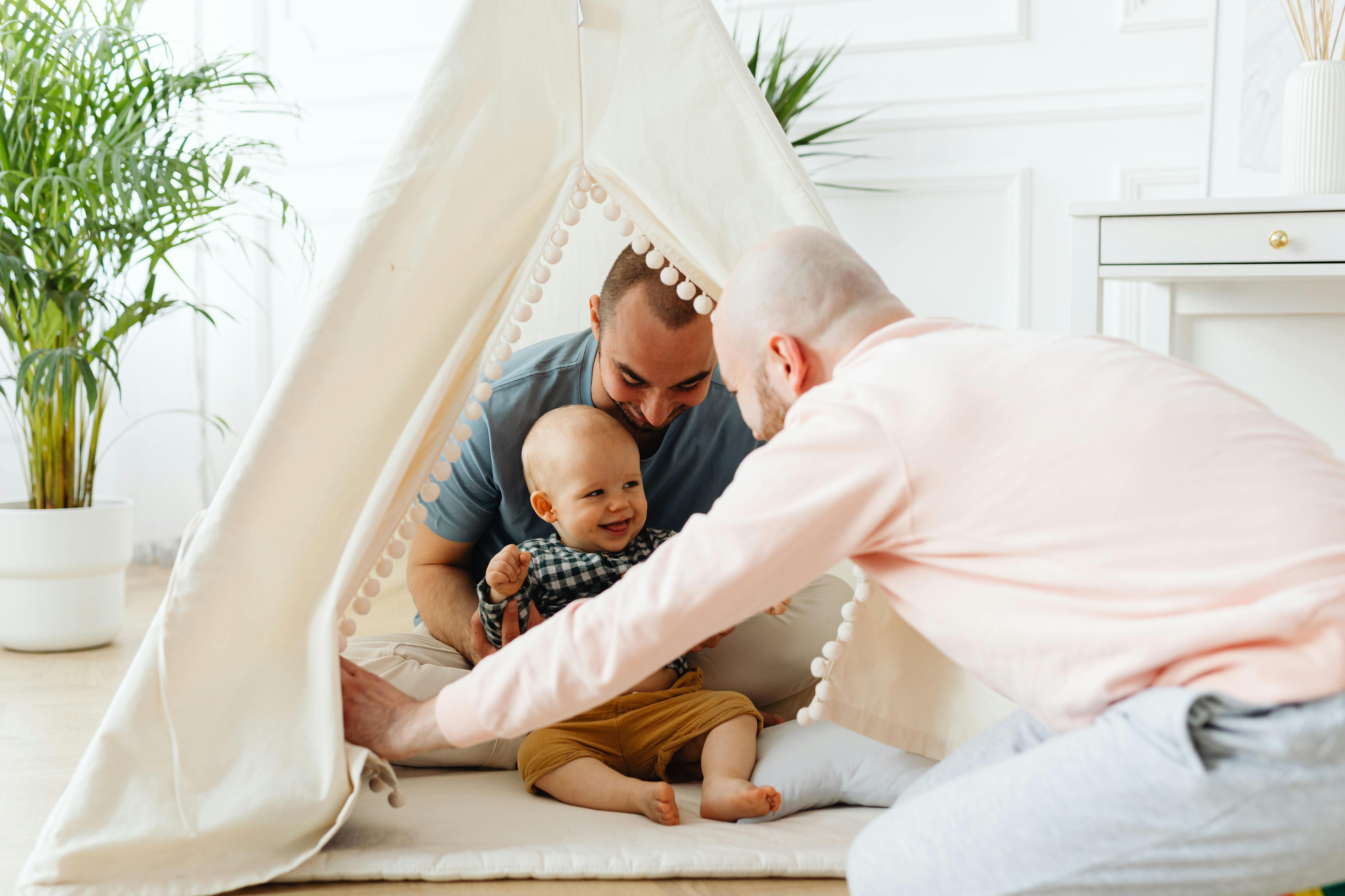 fathers playing with their baby in a childrens teepee tent set up in the living room